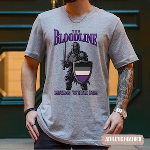 Puede incluir: Una camiseta gris con el texto "The Bloodline Ends With Me" impreso en ella. El dise&ntilde;o presenta un caballero con armadura sosteniendo una espada y un escudo. El escudo tiene los colores de la bandera del orgullo asexual.