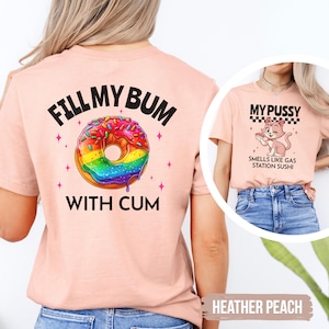Könnte beinhalten: Ein pfirsichfarbenes T-Shirt mit einer Grafik auf der Rückseite eines regenbogenfarbenen Donuts mit Streuseln und dem Text FILL MY BUM WITH CUM. Die Vorderseite zeigt eine Cartoon-Katze mit dem Text MY PUSSY SMELLS LIKE GAS STATION SUSHI.