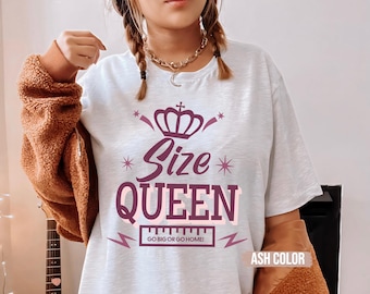 Pode incluir: Camiseta cinza claro com um gráfico de coroa bordô e as palavras "Size Queen". Abaixo está a frase "Go Big or Go Home!". A camiseta é cinza claro. O texto e os gráficos são bordô.