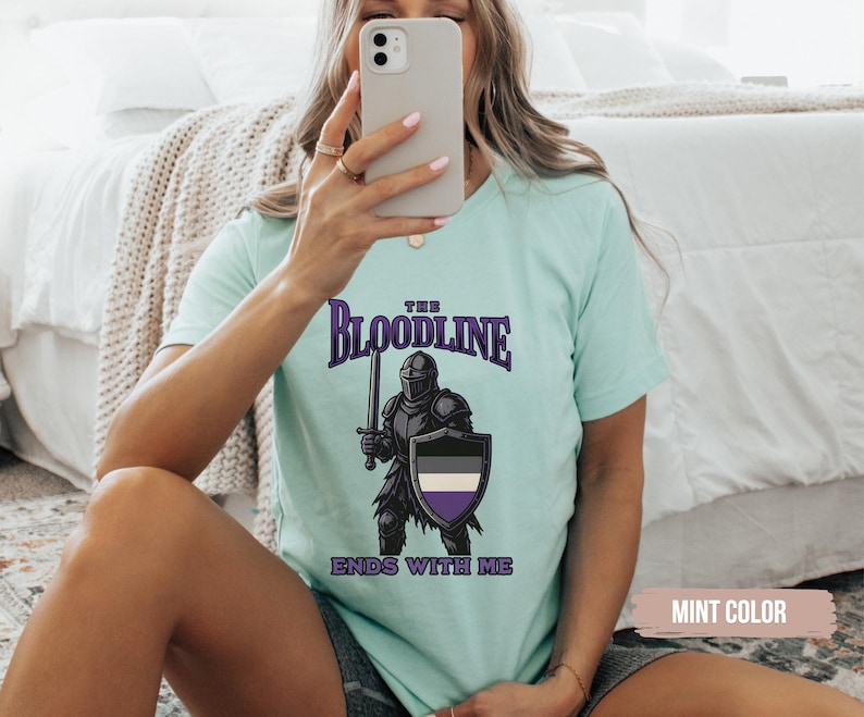 Puede incluir: Una camiseta azul claro con un gr&aacute;fico de un caballero sosteniendo una espada y un escudo. El escudo tiene un dise&ntilde;o negro, blanco y morado. El texto en la camiseta dice "The Bloodline Ends With Me".
