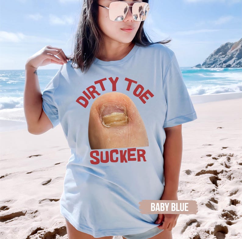Pu&ograve; includere: T-shirt azzurro con la scritta rossa "DIRTY TOE SUCKER" e una grafica di un dito del piede con un'unghia gialla. La maglietta &egrave; di colore azzurro.