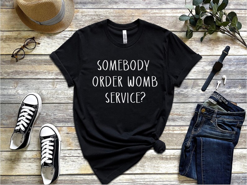 Op de afbeelding: Zwart T-shirt met witte tekst die "Heeft iemand een baarmoederdienst besteld?" zegt.