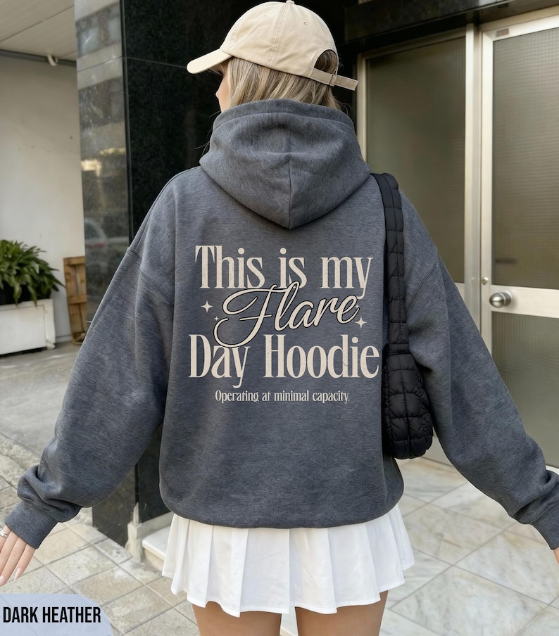 May include: Dark heather gray hoodie with the text "This is my Flare Day Hoodie" in a decorative font. The hoodie also has the text "Operating at minimal capacity" below the main text. The hoodie is part of a casual wear collection.