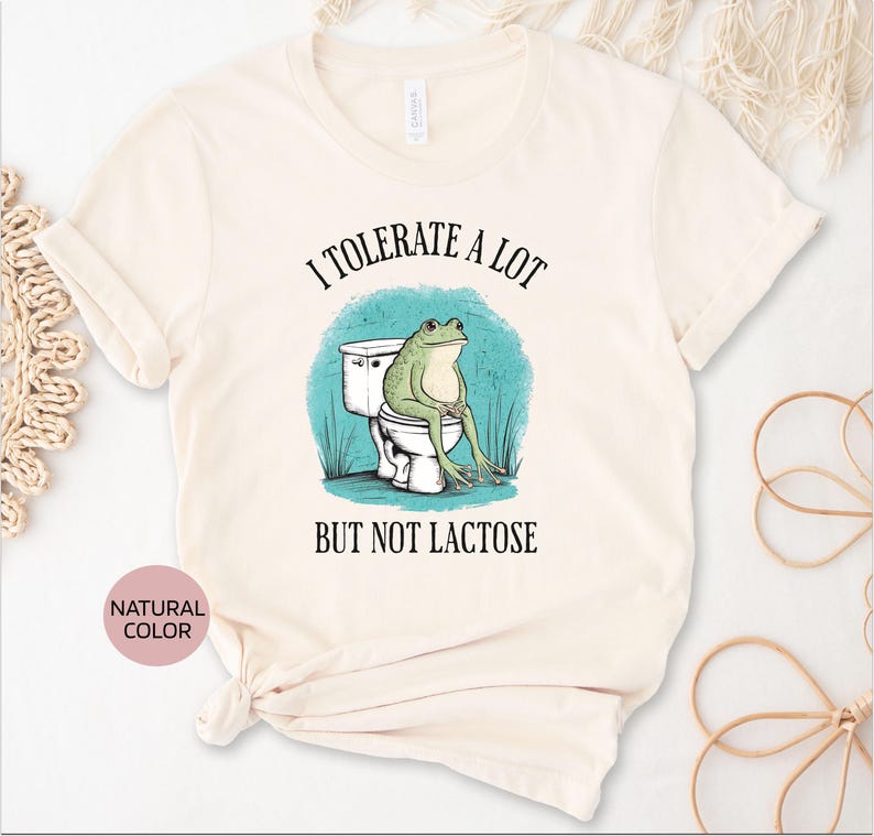 May include: A white t-shirt with the text "I tolerate a lot but not lactose" and a cartoon frog sitting on a toilet.