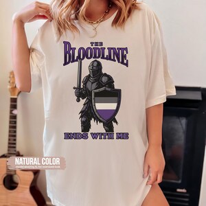 Puede incluir: Camiseta blanca con un gr&aacute;fico de un caballero sosteniendo una espada y un escudo. El escudo tiene los colores de la bandera del orgullo asexual. El texto "The Bloodline Ends With Me" est&aacute; impreso debajo del gr&aacute;fico.