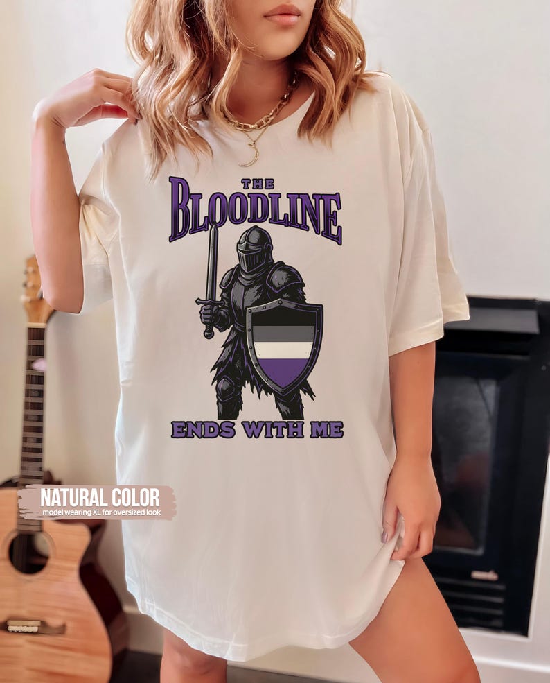 Puede incluir: Camiseta blanca con un gr&aacute;fico de un caballero sosteniendo una espada y un escudo. El escudo tiene los colores de la bandera del orgullo asexual. El texto "The Bloodline Ends With Me" est&aacute; impreso debajo del gr&aacute;fico.