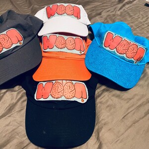 May include: Five baseball caps with the word "WEEN" in a stylized font on the front. The caps are in various colors, including black, white, orange, blue, and gray.