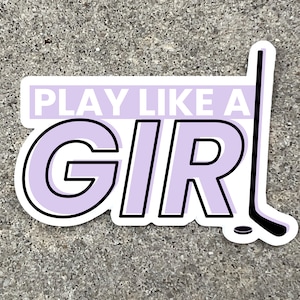 a 3 inch wide vinyl sticker with a purple and black design that reads play like a girl next to an image of a hockey stick is displayed on a stone background