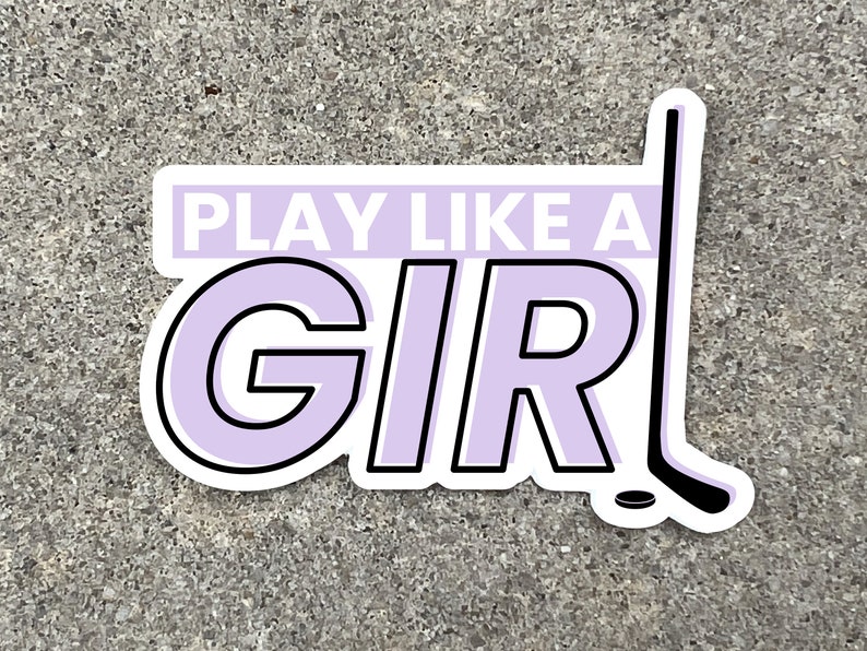 a 3 inch wide vinyl sticker with a purple and black design that reads play like a girl next to an image of a hockey stick is displayed on a stone background