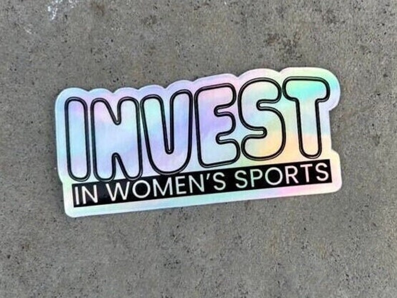 Puede incluir: Una pegatina hologr&aacute;fica con el texto "INVEST IN WOMEN'S SPORTS" en letras negras.