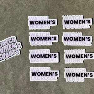 May include: Nine stickers with a purple background and black text. Each sticker says "Watch Women's" followed by a different sport: hockey, soccer, football, volleyball, basketball, rugby, lacrosse, and tennis. One sticker says "Watch Women's Sports".