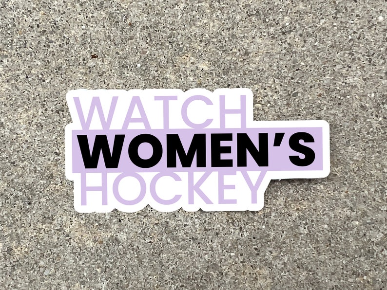 a 3 inch wide vinyl sticker with a purple and black design that reads watch womens hockey is displayed on a stone background