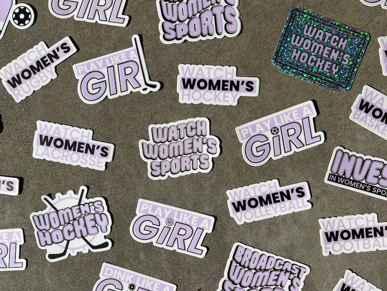 May include: A collection of stickers with various designs and text, including "Watch Women's Sports", "Play Like a Girl", and "Watch Women's Hockey". The stickers are purple and white with black text.