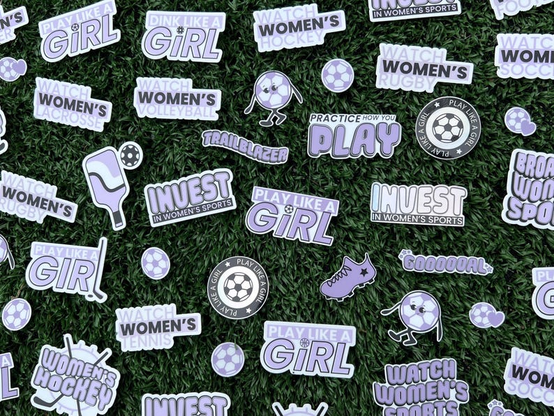Puede incluir: Una colecci&oacute;n de pegatinas con varios dise&ntilde;os de tem&aacute;tica deportiva. Las pegatinas son moradas y blancas con texto que dice "Play Like a Girl", "Watch Women's Hockey", "Invest in Women's Sports", y m&aacute;s.