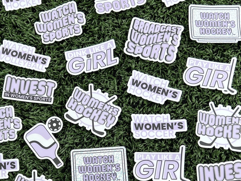May include: A collection of stickers with various slogans and designs related to women's sports. The stickers are purple and white with text such as "Watch Women's Hockey", "Invest in Women's Sports", and "Play Like a Girl".