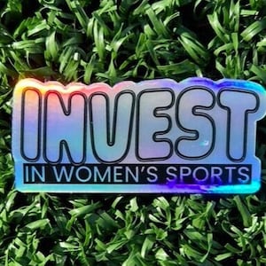 a 3 inch wide holographic vinyl sticker with a black outlined design that reads Invest in Womens Sports is displayed on a turf background