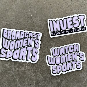 May include: Three stickers with a white background and black outlines. The stickers have purple text that reads "Broadcast Women's Sports", "Invest in Women's Sports", and "Watch Women's Sports".