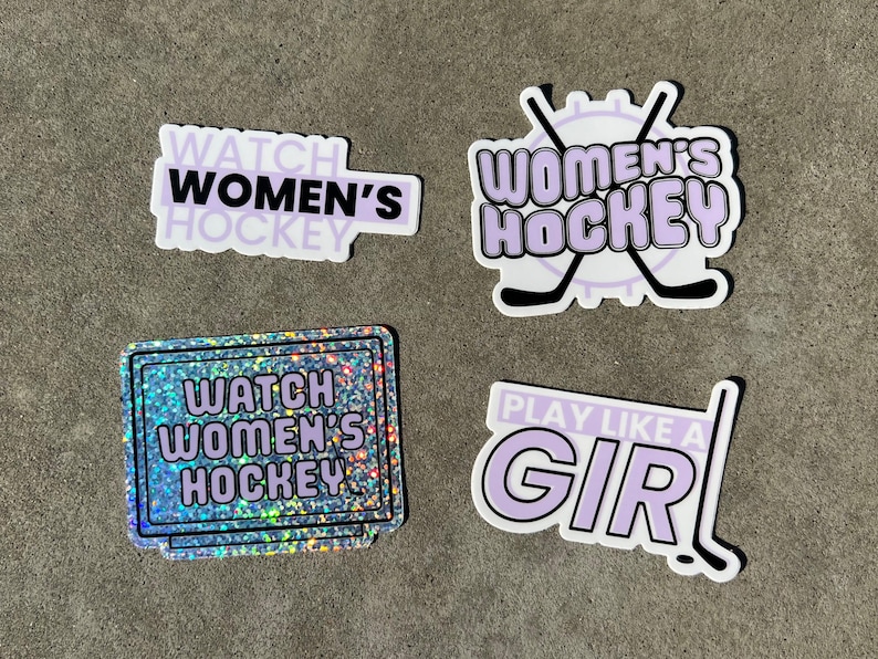 May include: Four stickers with a purple and white color scheme. The stickers feature the text "Watch Women's Hockey" and "Play Like A Girl!" with a hockey stick graphic. One sticker has a glittery background.