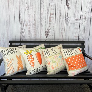 May include: Four decorative throw pillows with Easter-themed designs. The pillows feature bunnies, carrots, and the text "Bunny Trail", "He is Easter", and "Happy".