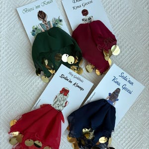 May include: Four cards with illustrations of women and text in Turkish, each paired with a colorful head covering adorned with gold sequins. The head coverings are in shades of green, burgundy, red, and navy blue.