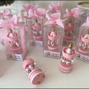 May include: Pink carousel favors with white and gold accents, presented in clear boxes tied with pink ribbons. Each carousel features a miniature horse and the text "Elif Alya 2 Yaşında".