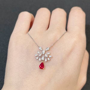 May include: A silver necklace with a teardrop-shaped ruby pendant surrounded by a cluster of smaller diamonds.