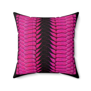 May include: A pink and black pillow with a geometric pattern resembling scales. The pillow is square and has a black border.