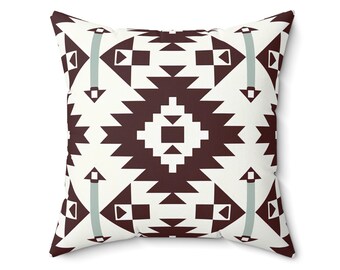 May include: Square throw pillow with a geometric pattern in shades of brown, white, and light blue. The design features repeating shapes, including triangles, squares, and arrows, creating a symmetrical and visually appealing pattern. The pillow is likely made of a soft fabric.