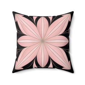 May include: A pink and black geometric cushion with a floral design. The cushion has a black background with a pink flower in the centre. The flower has a symmetrical design with multiple petals.