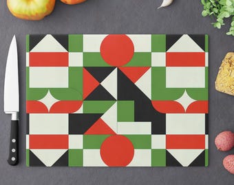 May include: Rectangular cutting board with a geometric pattern in red, green, black, and cream. The design features circles, squares, triangles, and diamond shapes. A stainless steel knife and fresh produce surround the board.
