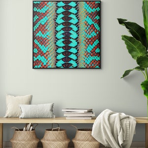 Könnte beinhalten: Ein gerahmter Druck eines türkisfarbenen und braunen Schlangenhautmusters. Der Druck hängt an einer hellgrünen Wand über einer Holzbank mit zwei beigen Kissen, einem Stapel Büchern und drei geflochtenen Körben.