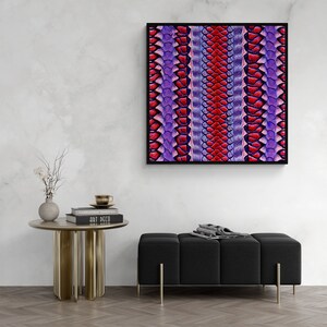 Könnte beinhalten: Ein gerahmter Druck eines farbenfrohen abstrakten Musters mit lila und roten Schuppen. Der Druck hängt an einer weißen Wand über einem schwarzen Ottoman und einem goldenen Beistelltisch mit Büchern darauf.