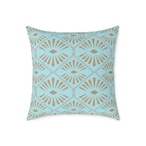 May include: Square throw pillow with a geometric pattern. The pillow features a light blue background with a repeating design of tan fan-like shapes and diamond outlines. The pillow is a decorative accent for a sofa or bed.
