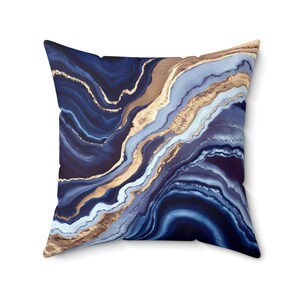 May include: Blue and gold abstract throw pillow with a marbled design. The pillow features a swirling pattern of blue and gold, reminiscent of agate.