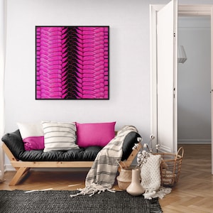 Könnte beinhalten: Ein quadratischer Druck in einem schwarzen Rahmen mit einem abstrakten Muster in Pink und Schwarz hängt an einer weißen Wand über einem schwarzen Futon mit weißen und rosa Kissen. Der Futon befindet sich in einem Wohnzimmer mit einem weißen Teppich, einem Holzboden und einer weißen Tür.