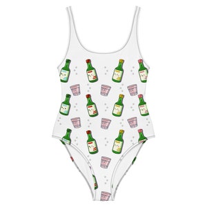 May include: White one-piece swimsuit with a pattern of green bottles and pink glasses. The bottles and glasses have cartoon faces.