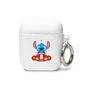 May include: White Airpod case with a blue Stitch character from Lilo & Stitch driving a red spaceship. The case has a silver metal ring attached.