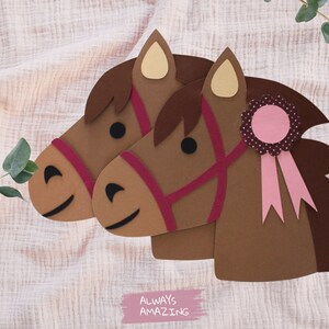May include: Two brown paper horse heads with pink and red details. The horse on the right has a pink ribbon with a pink and white polka dot rosette. The text "ALWAYS AMAZING" is written in pink on a white background.