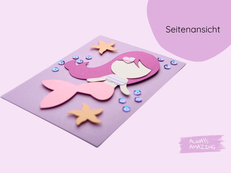 Op de afbeelding: Een paarse kaart met een papieren uitsnijding van een zeemeermin met roze haar, een roze staart en een wit topje. De zeemeermin is omringd door roze en blauwe glitters en oranje zeesterren.