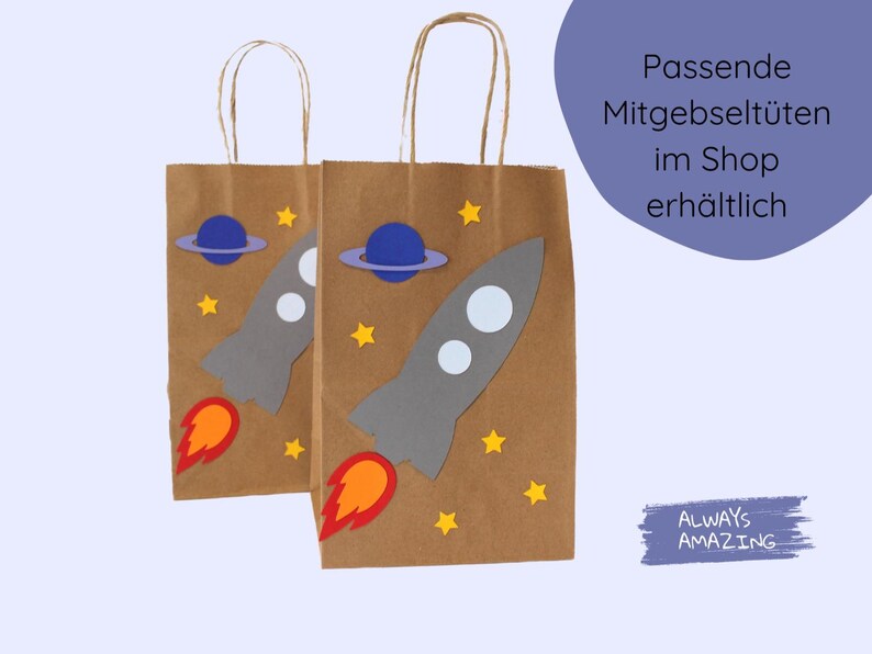 May include: Two brown paper gift bags with handles. Each bag has a rocket ship, planets, and stars cut out of colored paper and glued on. The text "Passende Mitgebselt&uuml;ten im Shop erh&auml;ltlich" is on the right side of the image.