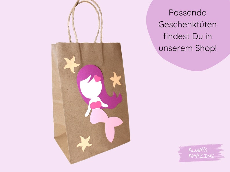 Op de afbeelding: Een bruine papieren cadeauzak met een zeemeerminontwerp. De zeemeermin is gemaakt van roze, paars en wit papier. De tas heeft een wit handvat en is versierd met gele papieren sterren. De tekst "Passende Geschenkt&uuml;ten findest Du in unserem Shop!" is zichtbaar in de rechterbovenhoek van de afbeelding. De tekst "ALWAYS AMAZING" is zichtbaar in de rechterbenedenhoek van de afbeelding.