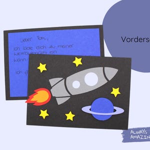May include: A black card with a rocket ship, stars, and a planet with rings. The text "Lieber Tom, Ich lade dich zu meiner Weltraumparty ein Wann Ich fo" is written on the blue card behind it. The text "Vorderseite" is written on a blue circle above the card. The text "ALWAYS AMAZING" is written on a blue rectangle below the card.