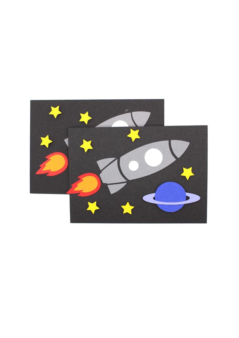 May include: Two black cards with a gray rocket ship, a blue planet with a ring, and yellow stars. The rocket ship has a red and orange flame.