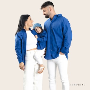 May include: A family of three wearing matching blue shirts. The parents are looking at each other, while the child is being held by the mother. The child is wearing a blue bandana with a white pattern.