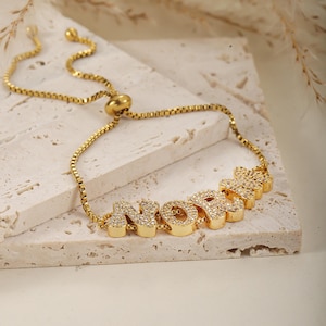 Peut inclure: Bracelet ajustable en or avec le mot "NORMA" écrit en grandes lettres incrustées de zirconiums cubiques.