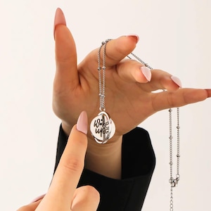 May include: A silver-colored necklace with a pendant that reads "Wake Upon". The pendant is a circular design with a rotating outer ring. The necklace chain has small, round beads. The background is white.