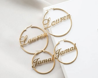 May include: Two pairs of gold hoop earrings with the names "Lauren" and "Jamal" written in cursive on them.