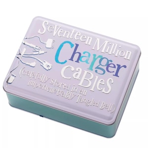 Può includere: Una scatola di latta di colore lilla chiaro con un design blu e bianco. Il testo sulla scatola recita "Seventeen Million Charger Cables (carefully stored in an impenetrably tangled ball)".