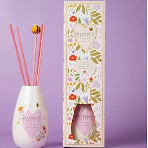 May include: A white ceramic essential oil diffuser with pink reeds and a decorative bee topper. The diffuser has a heart-shaped design with the word "Mummy" and the phrase "love you so much". The packaging features floral patterns.