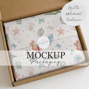 May include: A brown cardboard shipping box containing tissue paper with a repeating pattern of seashells, starfish, coral, and small bows in soft blue, peach, and green tones. A circular white sticker with the text That's the One seals the paper.